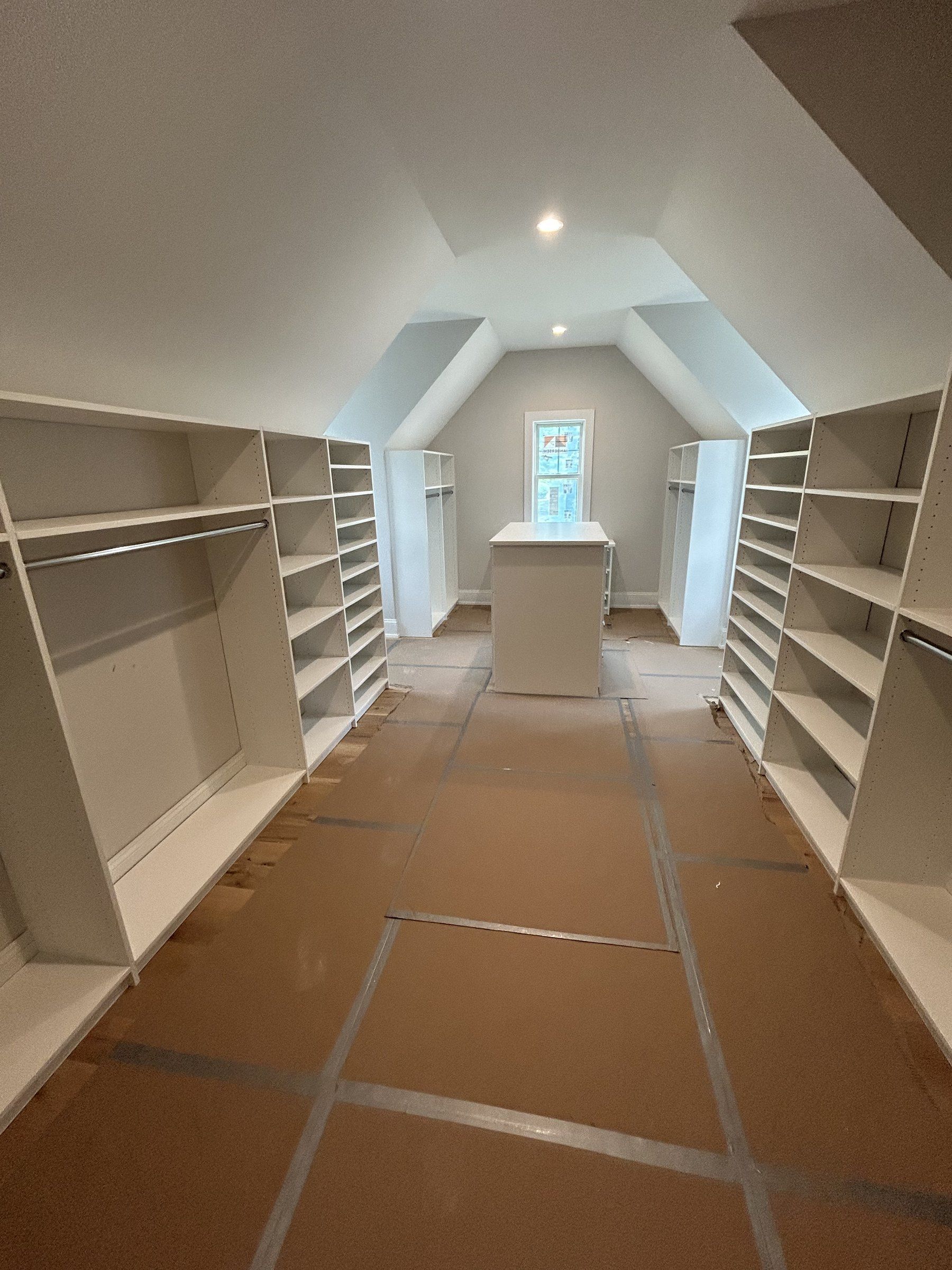 Long attic walk-in closet built under a sloped ceiling with an island at the far end