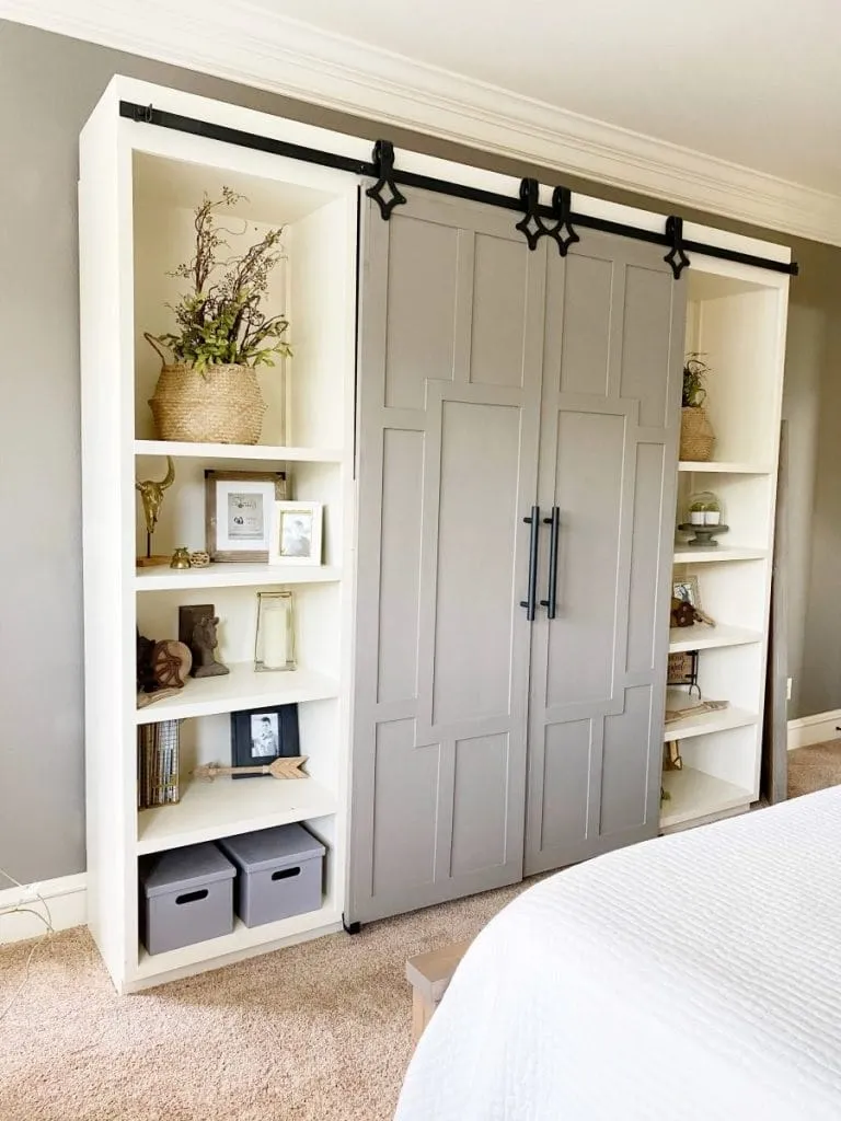 Built-in white bookshelves with gray sliding barn doors and black hardware in a bedroom