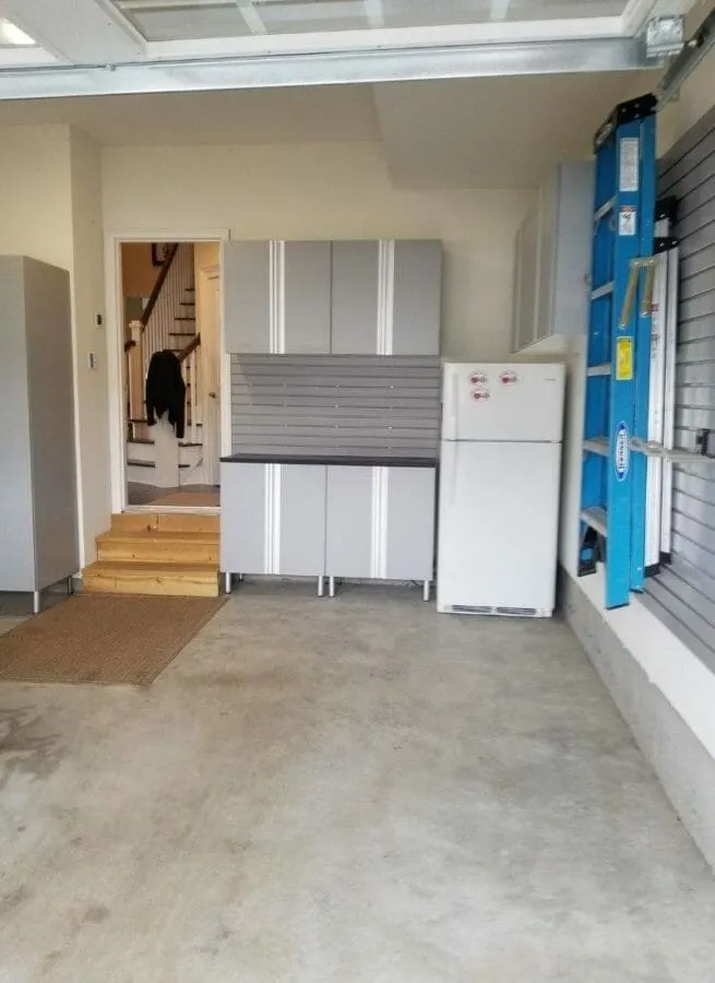 Modern garage setup with gray cabinets, refrigerator, and tool storage for functional workspace organization.