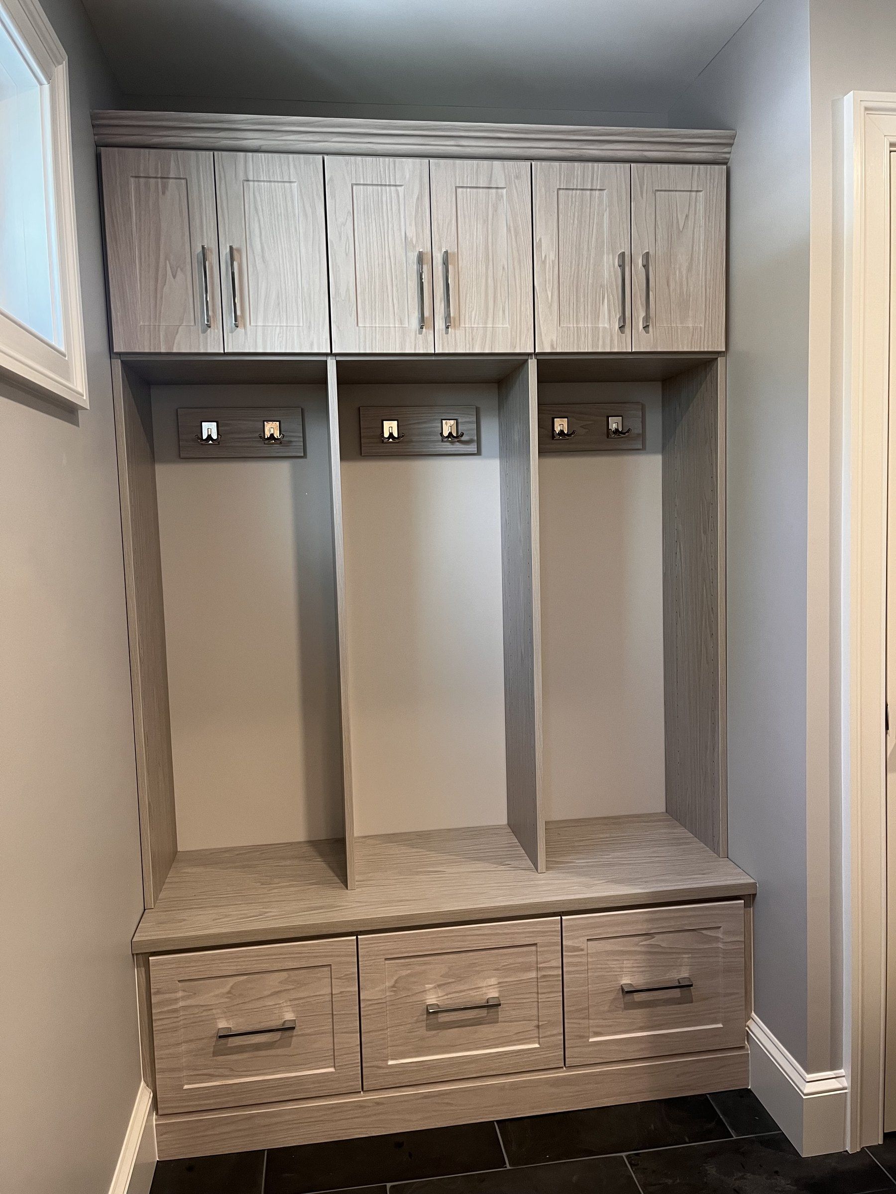 Gray wood-grain mudroom lockers with hooks, upper cabinets and bench drawers