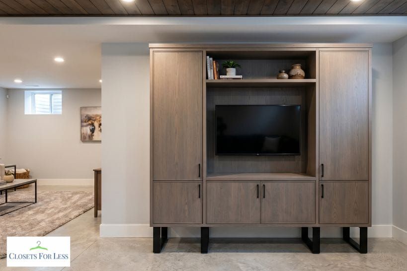 Custom basement cabinet with built-in TV storage, wood doors, black hardware, and modern entertainment shelving.