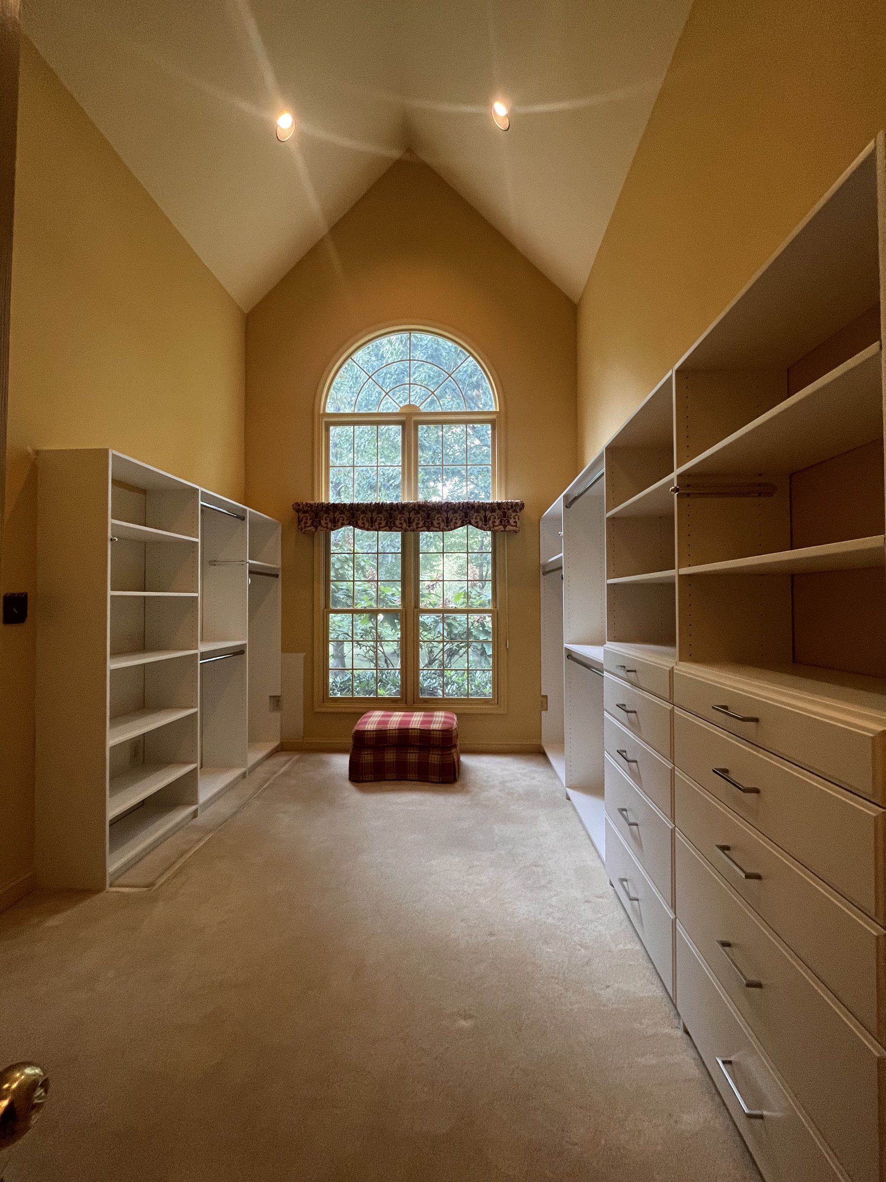 Long walk-in closet with a vaulted ceiling, arched window and floor-to-ceiling shelving