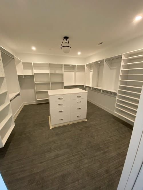 White custom walk-in closet with built-in shelving, drawers, and center storage island