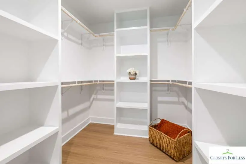 Empty walk-in closet with white built-in shelving, corner hanging rods, and wood flooring, featuring a woven basket on the floor.