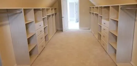 Long walk-in closet with matching built-in shelving, drawers, and hanging rods on both sides, finished with carpet and a doorway at the end.
