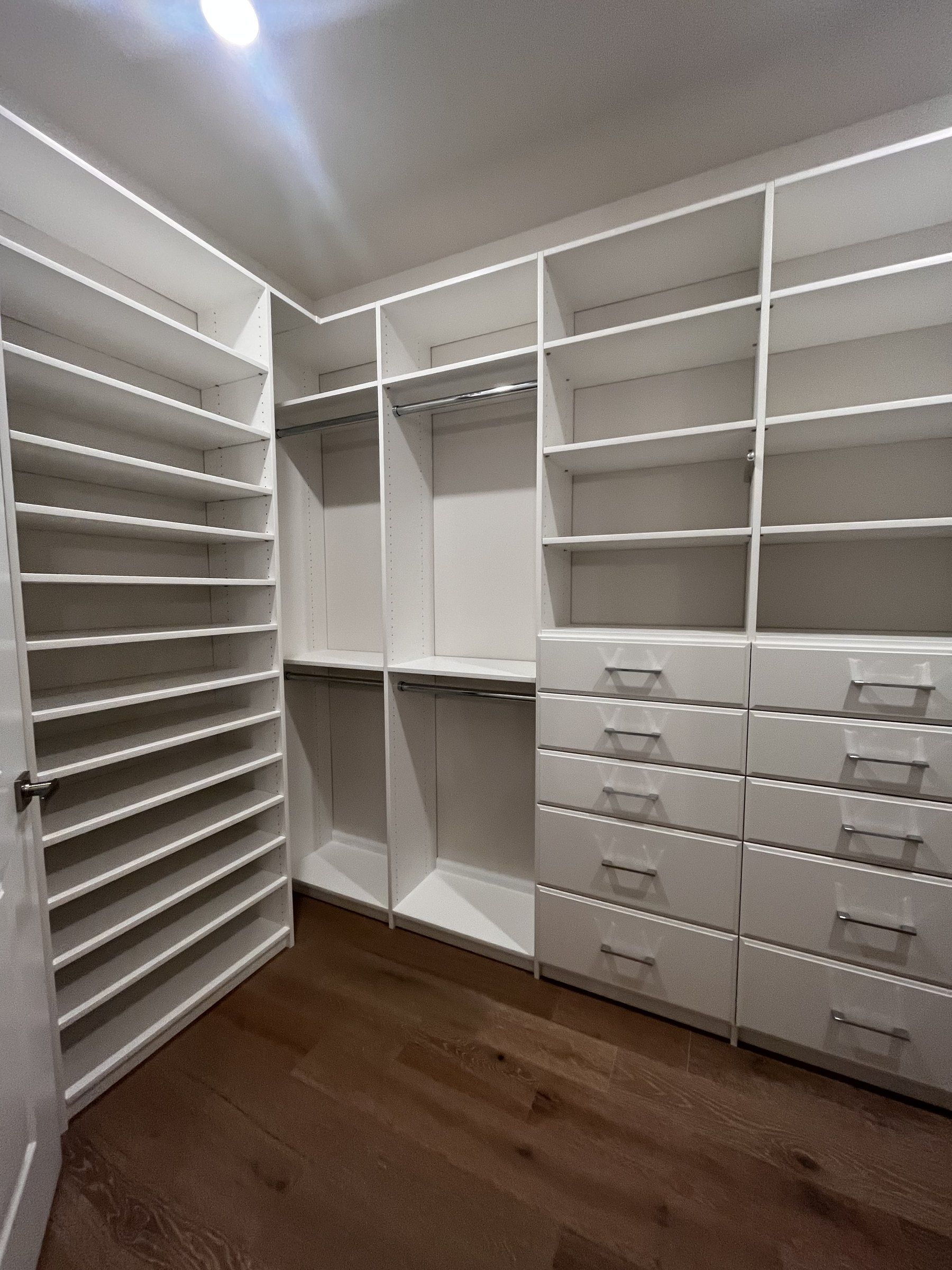 White walk-in closet with angled shoe shelves and a bank of drawers